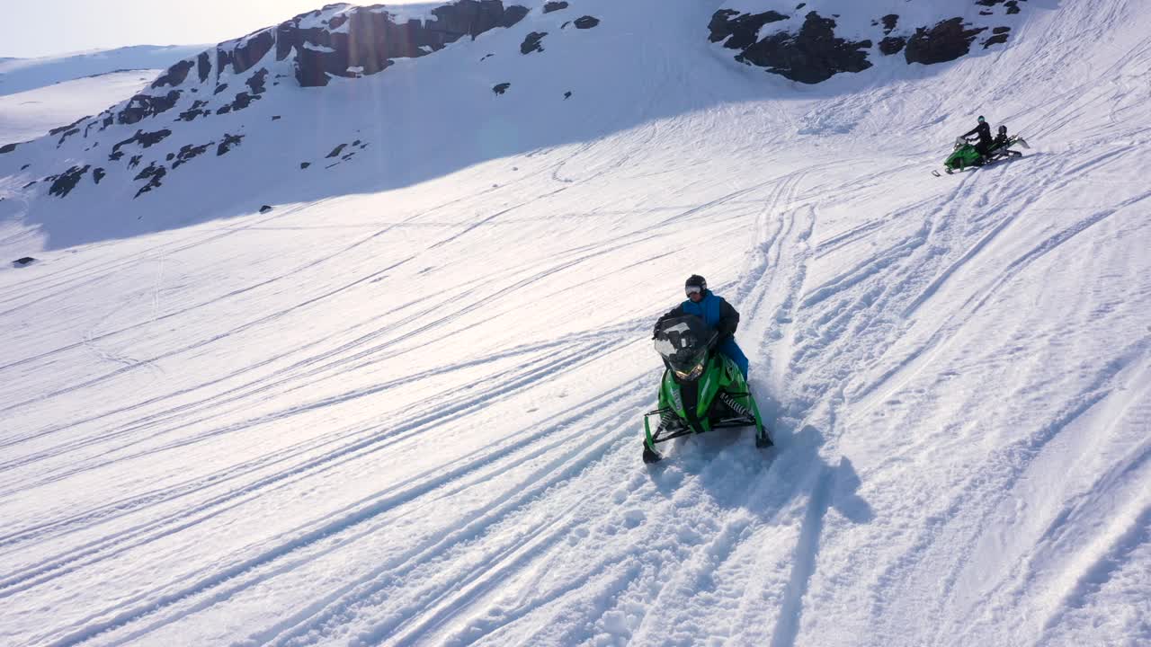 Aerial view over snowy mountain landscape. Snowmobile passing under. Sunny weather. MOVING UP.