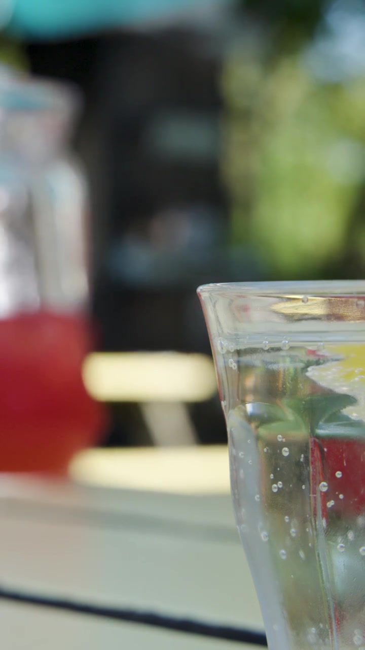 A hand grabs a red cocktail next to sparkling water on a sunlit outdoor table