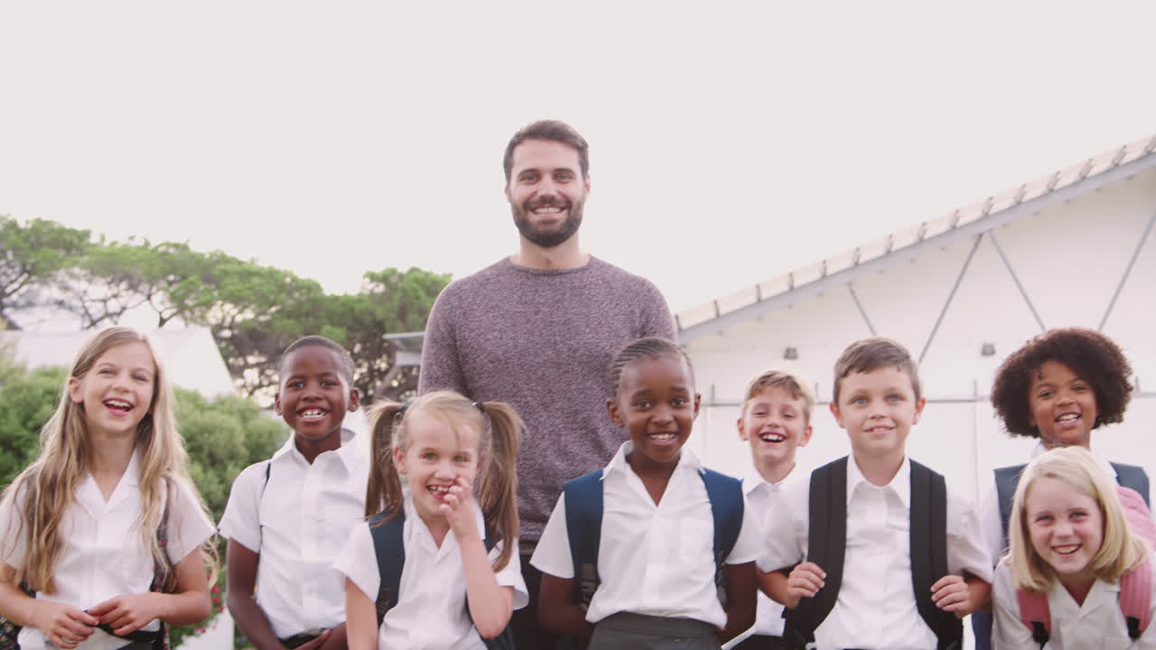 Outdoor Portrait Of Elementary School Pupils With Teacher Wearing Uniform Standing On Playing Field