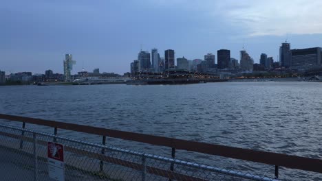 Skyline-Von-Montreal-In-Der-Abenddämmerung-Von-Der-Anderen-Seite-Des-Wassers-Mit-Einem-Parkzaun-Im-Vordergrund