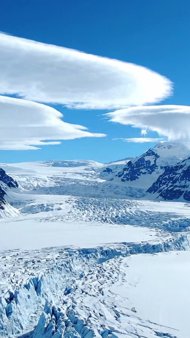 Et fantastisk isbrelandskap med majestetiske isformasjoner og dramatiske skyformasjoner under en klar blå himmel