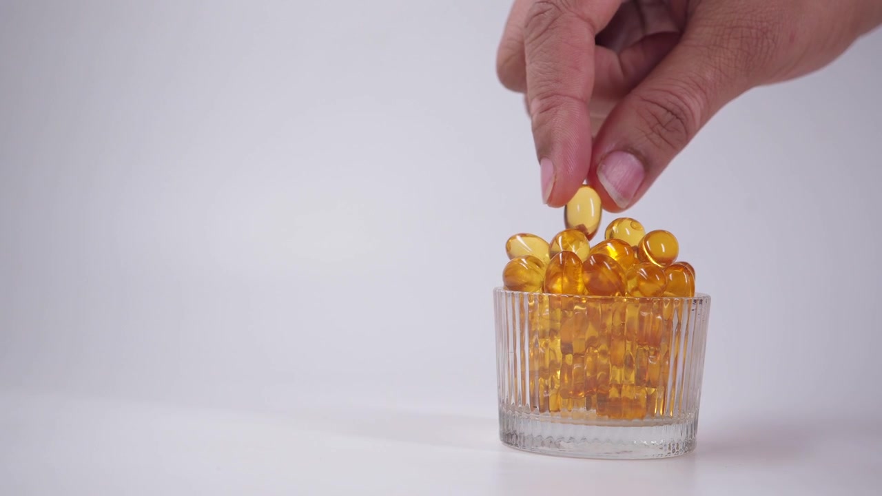 Tangan Mengambil Kapsul Omega-3 Emas dari Mangkuk Kaca