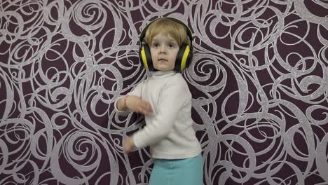 Little-happy-child-jumping-and-dancing-on-sofa-and-listening-music-in-headphones