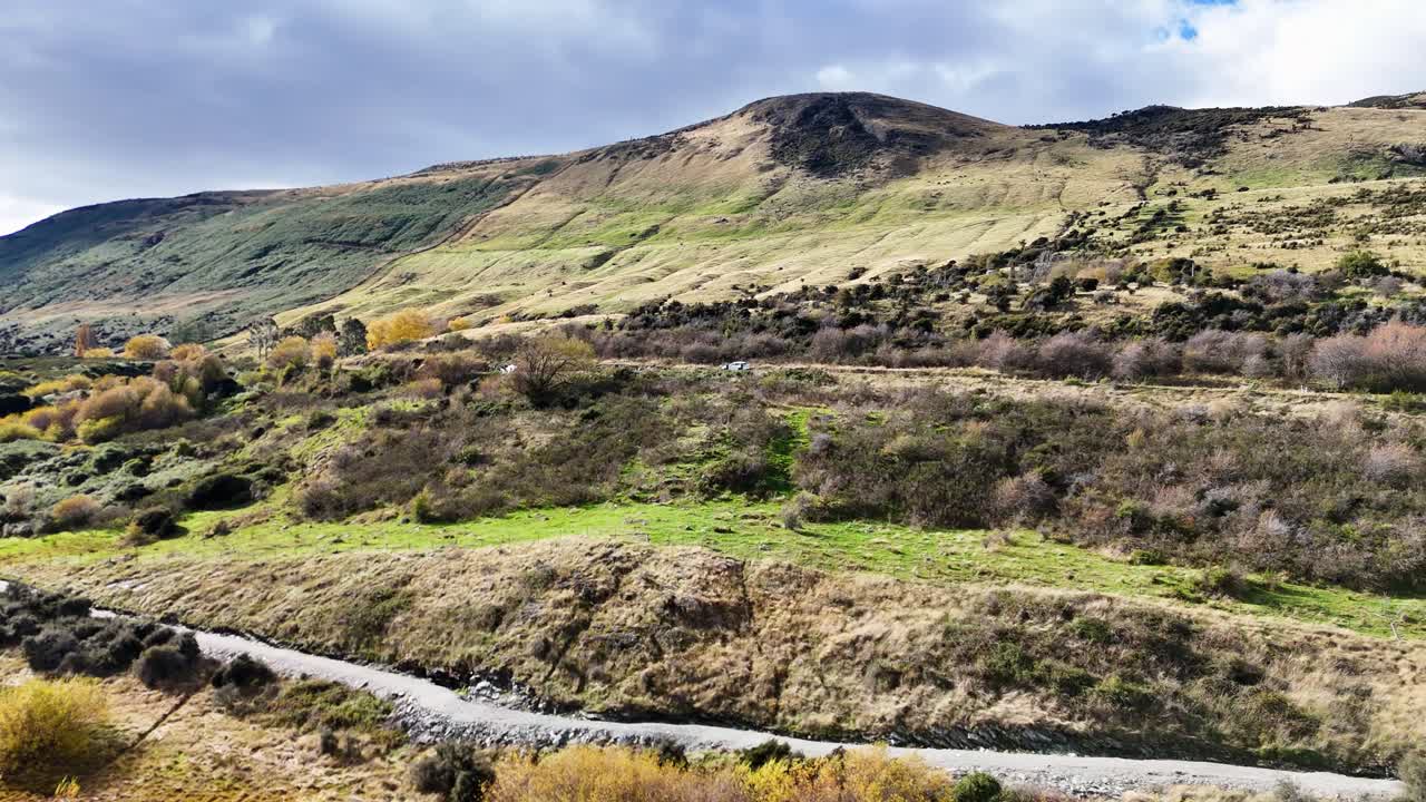 Aerial footage captures the lush, rolling hills of Queenstown, New Zealand, under soft, natural lighting with a serene atmosphere