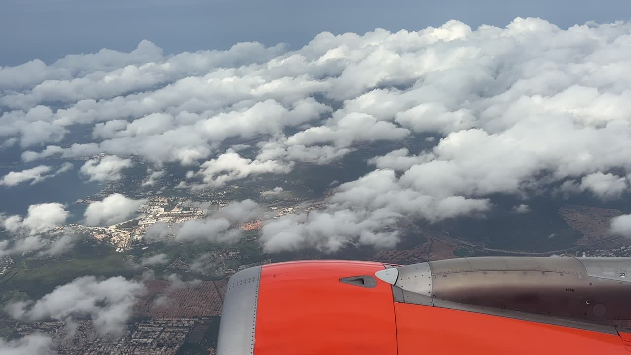 Aerial view from airplane window showing clouds and Mallorca island landscape below