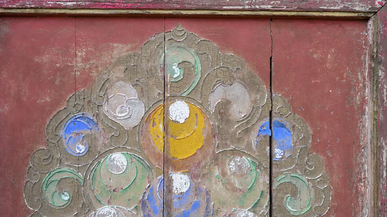 Close-up of ancient painted wood detail at Erdene Zuu Monastery in Kharkhorin, Mongolia. The weathered red surface features faded traditional Buddhist patterns, highlighting historic artistry