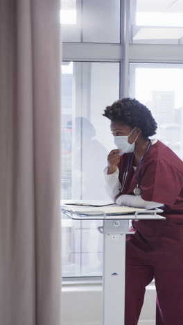 vertical video of african american female doctor talking in hospital room, slow motion