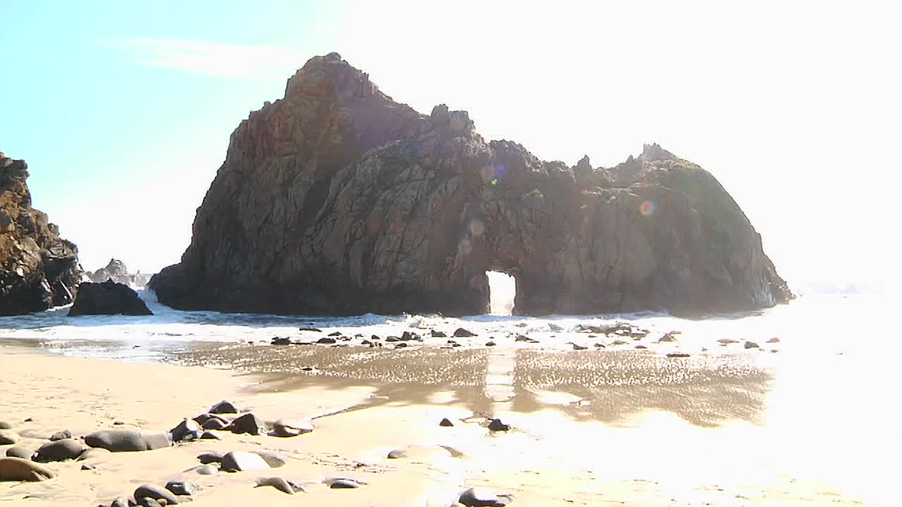 아치 바위 전경이 있는 캘리포니아 해안선을 따라 화창한 날 파도가 해안으로 굴러 들어옵니다.