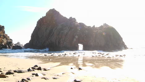 waves roll into shore on a sunny day along california coastline with an arch rock foreground