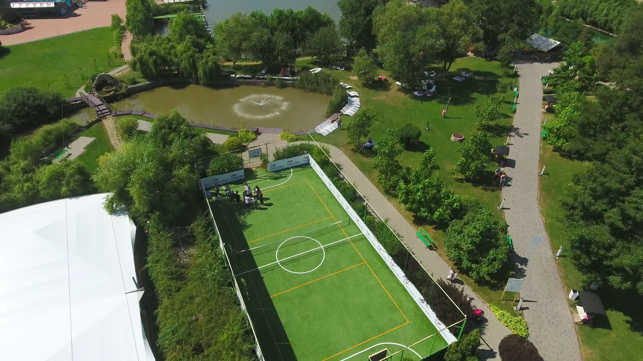 People resting at spa recreational complex in rural area. Green beautiful territory with swimming-pool, tennis court and pond with fountain. Drone footage.