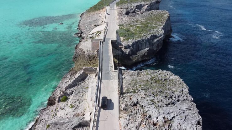 Filmische Drohnenaufnahme aus der Luft, die einem Auto folgt, das eine Glasbrücke auf der Insel Eleuthera auf den Bahamas überquert – die den Atlantik vom Karibischen Meer trennt.