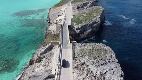 vista aérea cinematográfica tomada por un avión no tripulado siguiendo a un automóvil que cruza el puente de ventanas de vidrio en la isla de eleuthera en las bahamas, que separa el océano atlántico del mar del caribe