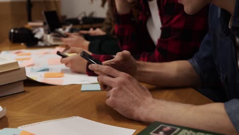 Zugeschnittene-Aufnahmen-Von-Vier-Studenten,-Die-In-Der-Pause-Gemeinsam-Am-Tisch-Sitzen-Und-Mit-Smartphones-SMS-Schreiben,-Im-Internet-Surfen,-Während-Sie-In-Der-Uni-Bibliothek-Sitzen