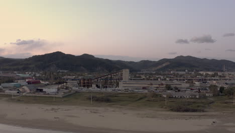 Concrete-making-factory-industrial-complex-near-seaside-in-the-evening-with-town-buildings-in-the-background,-Far-East,-Russia