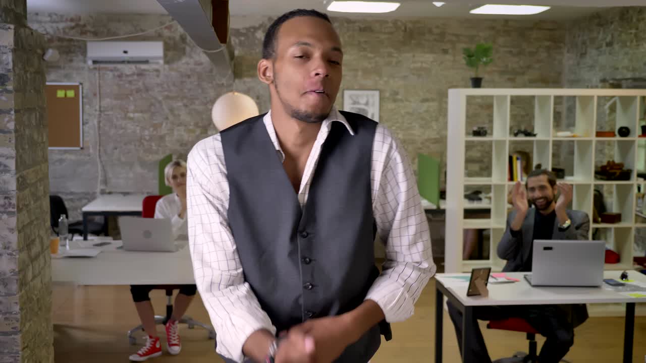 Young african businessman is dancing in office, colleagues are clapping, work concept, relax concept, movement concept