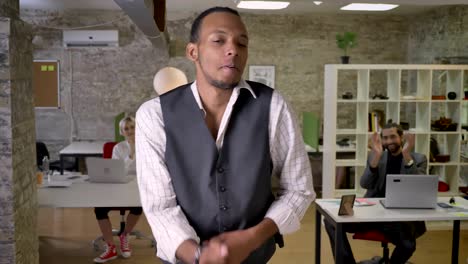young african businessman is dancing in office, colleagues are clapping, work concept, relax concept, movement concept