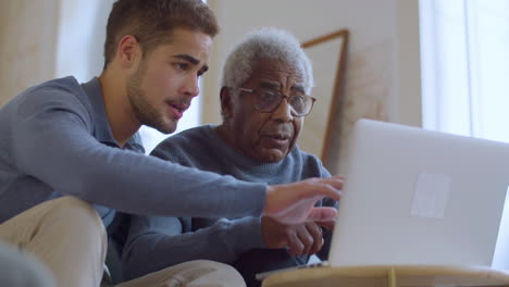 bearded caucasian guy helping senior black man with using laptop