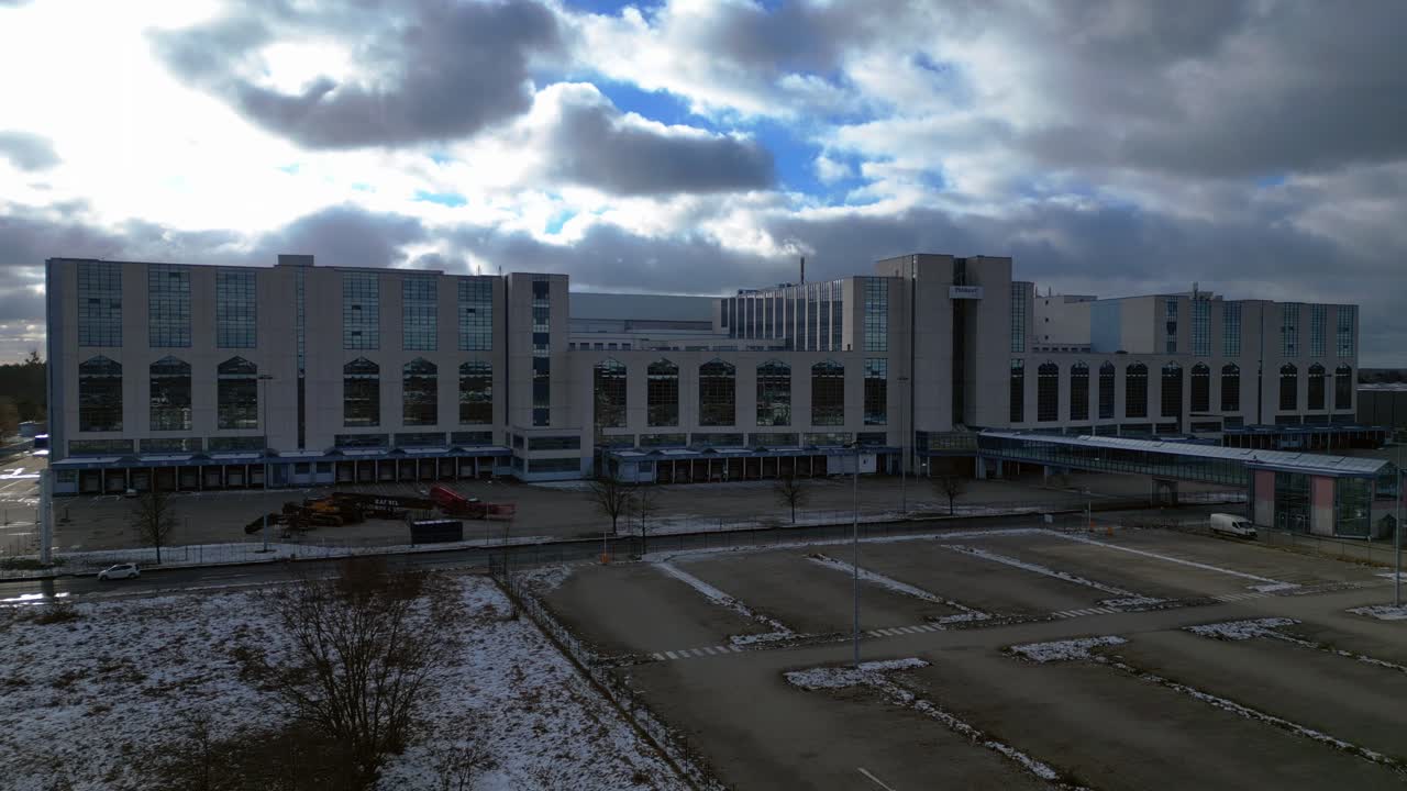 Large distribution center with loading docks and parking lot under a cloudy sky in winter. Majestic aerial view flight static tripod hovering drone
