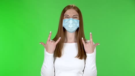 portrait of pretty young girl in medical protective face mask looking at camera and making a rock gesture with both hands