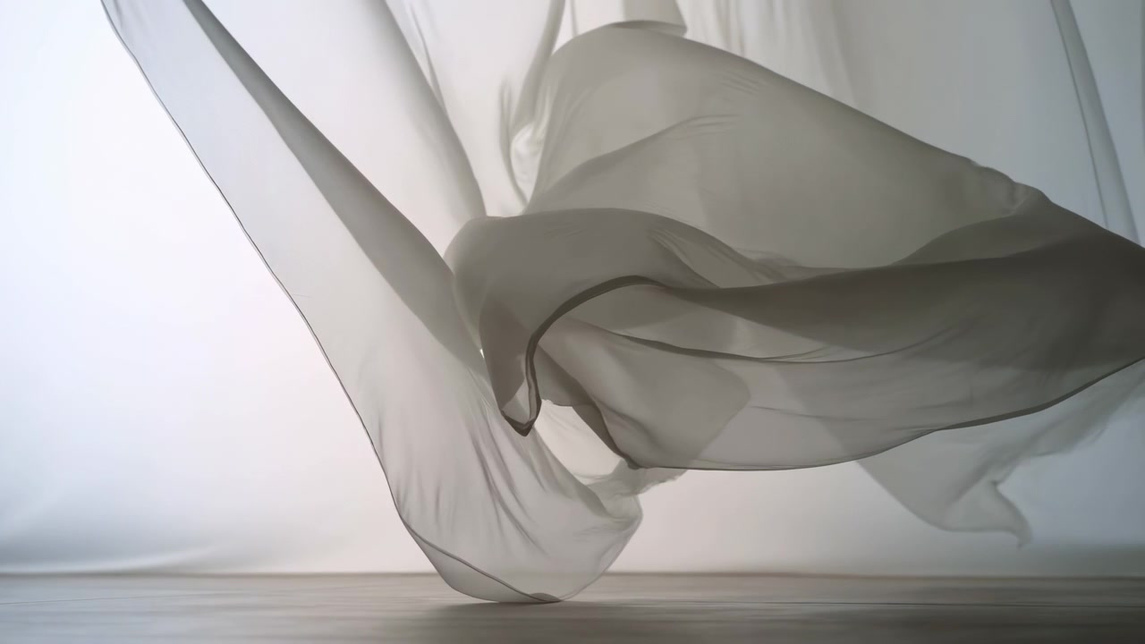 Sheer chiffon panels move through layered shapes over smooth studio floor in minimal setting, lifting, drifting, folding, then settling into soft curls with delicate light and shadow