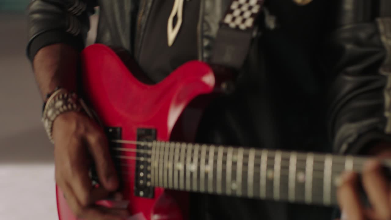 Un chitarrista in primo piano durante l'esibizione. La chitarra elettrica è rossa e il chitarrista indossa una giacca nera da rockstar, con il resto della band sullo sfondo