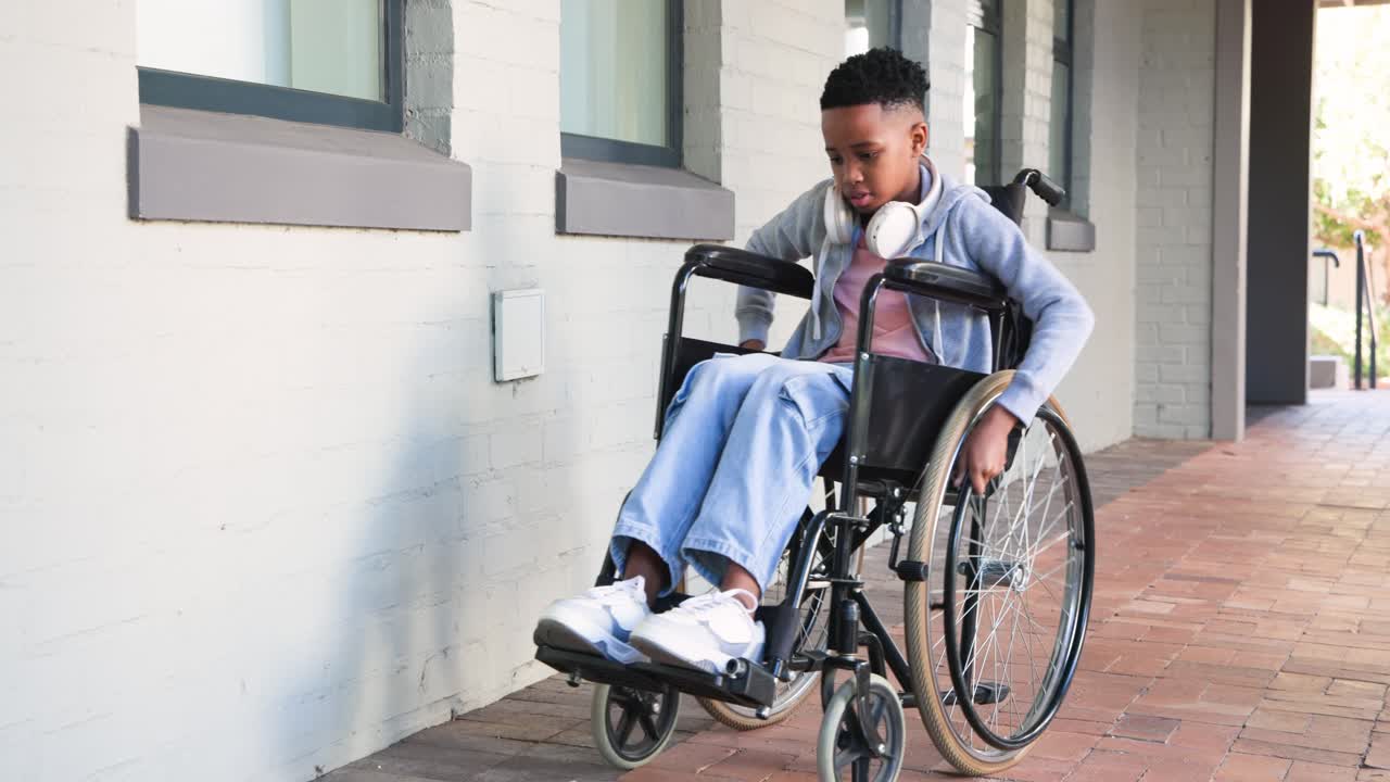 African American male teen leaning pushing wheelchair along covered walkway smiling at camera