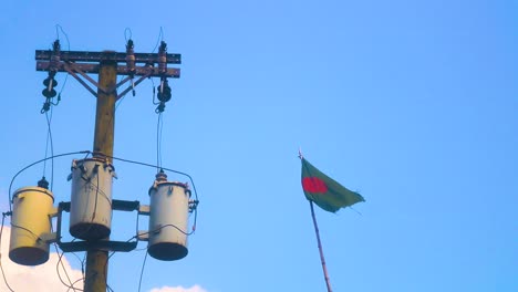 la bandera de bangladesh ondea junto a un transformador eléctrico en un día de cielo azul claro