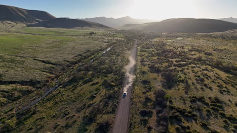 Aerial-shot-of-car-driving-towards-camera-on-dirt-road-in-Willcox,-Arizona,-wide-drone-shot-with-mountains-in-the-background-and-dust-behind-the-car