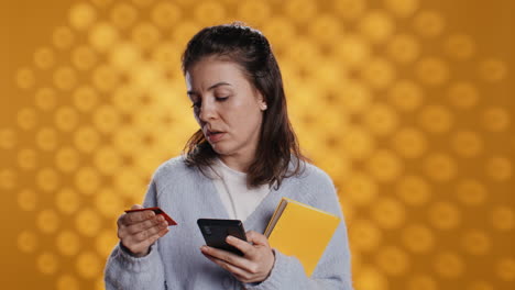 Woman-holding-books,-purchasing-more-with-phone,-studio-background