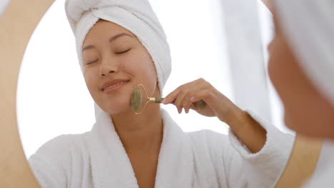 mujer usando un rodillo de jade para masaje facial