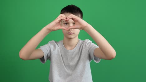 boy hands making heart shape gesture on green screen chromakey background. person forms heart shape using their fingers