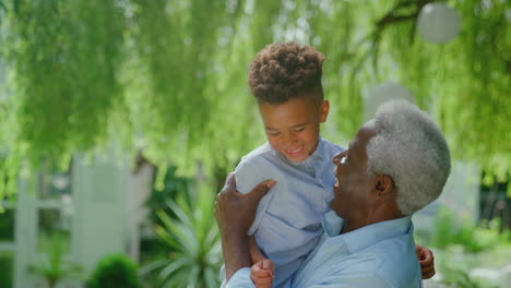 Portrait-Of-Loving-Grandfather-Holding-Grandson-In-Arms-In-Garden-At-Home