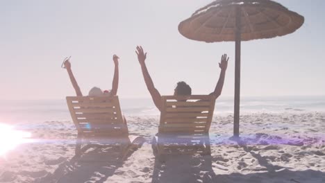 Animation-of-light-spots-over-caucasian-couple-raising-hands-at-beach