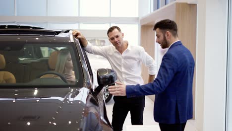 Blonde-sitting-inside-the-car-during-visit-auto-dealership,-listening-with-husband-to-consultant