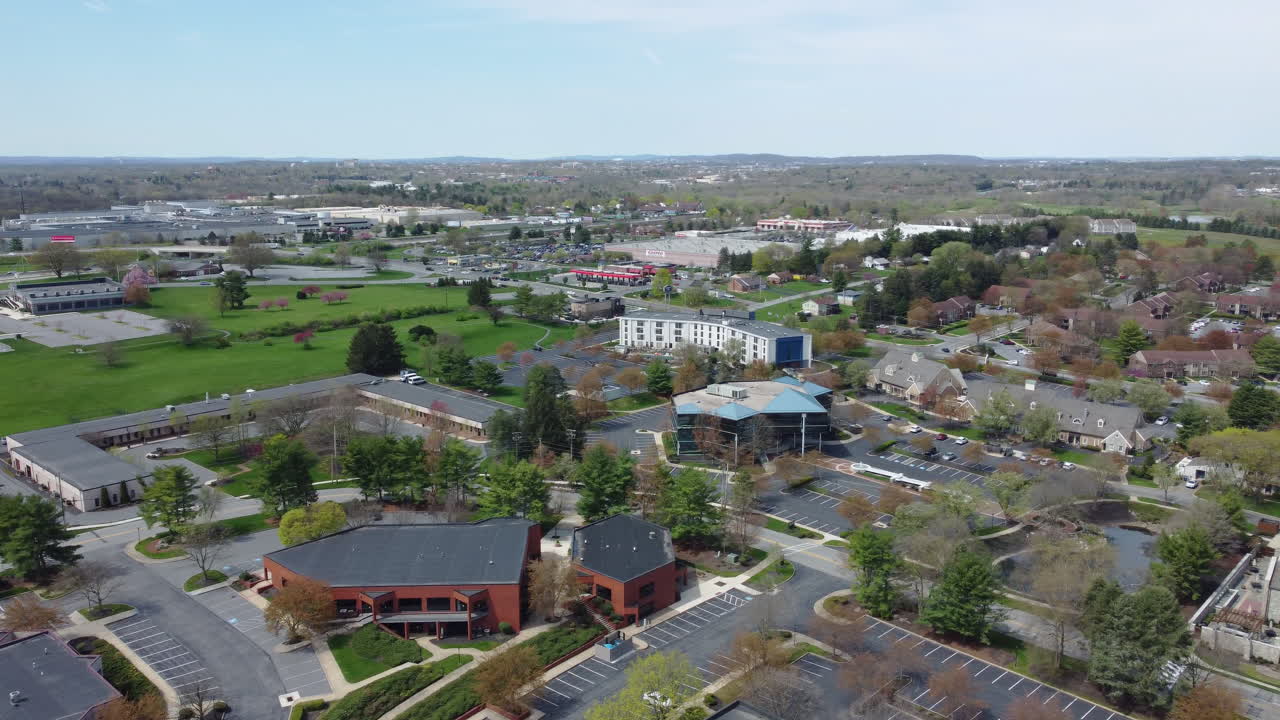 A sweeping drone pan captures both a Lancaster, PA commercial office park and neighboring residential community, with a vast backdrop of Lancaster County’s fields, rooftops, and springtime greenery.