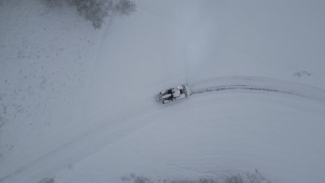 Tractor-plowing-snow-on-rural-countryside-road-in-winter,-ascending-top-down-aerial-view