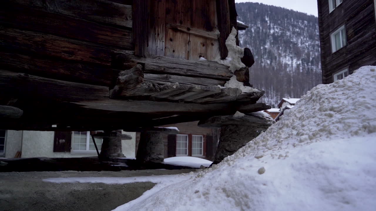 Panning past bottom side of old cabin in small town in Switzerland