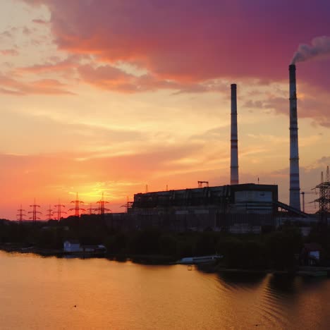 harmful factory against pink sky at sunset. smoke from the industrial chimney pollute the environment. chemical plant near the evening river.