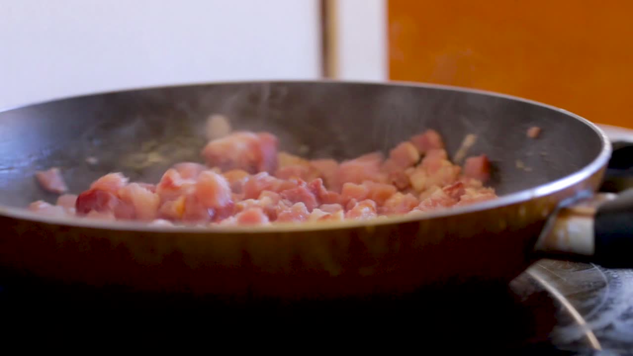 Bacon is cooked and stirred in a frying pan