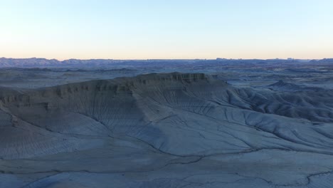 aerial view flying over moonlike landscape, dry desert land and hills under factory butte during twilight