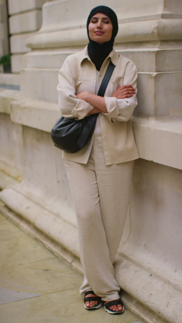 Vertical Video Portrait Of Smiling Muslim Businesswoman Wearing Hijab And Modern Business Suit Standing And Folding Arms Outside City Office Buildings 4