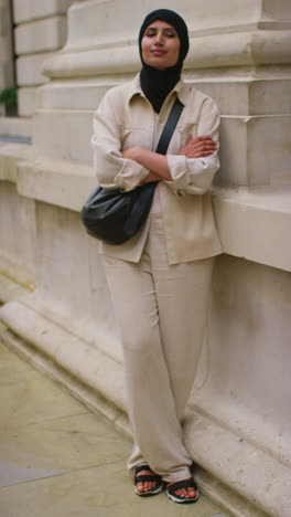 Vertical-Video-Portrait-Of-Smiling-Muslim-Businesswoman-Wearing-Hijab-And-Modern-Business-Suit-Standing-And-Folding-Arms-Outside-City-Office-Buildings-4