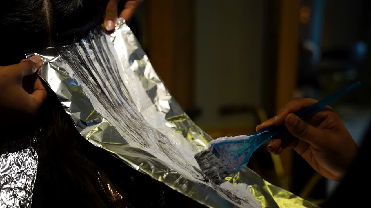 Penata rambut mengaplikasikan pewarna dengan kuas ke bagian rambut yang ditempatkan di atas aluminium foil selama perawatan salon