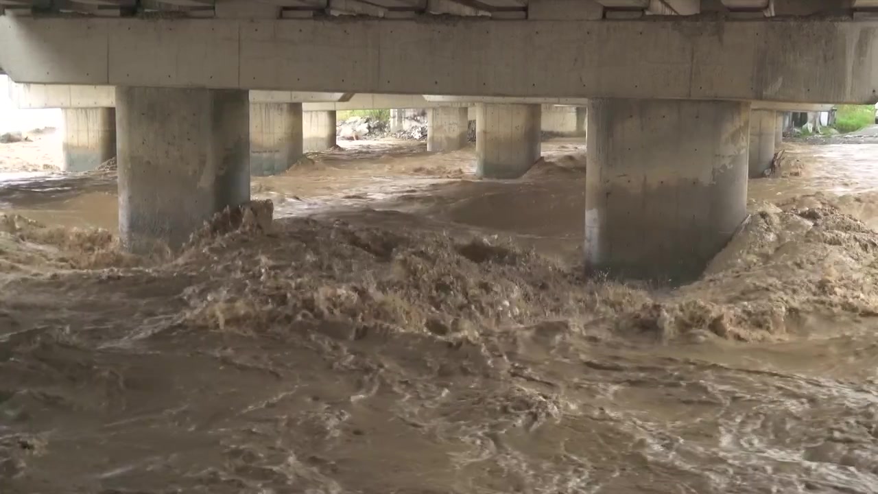 Agua turbia de inundación corriendo bajo pilares de puente de hormigón.