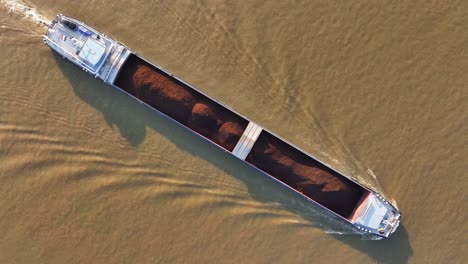 wide top down aerial of long freighter ship transporting coal on brown water