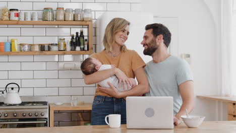 retrato de la familia en la cocina en el desayuno con la madre cuidando al hijo bebé y el padre usando una computadora portátil