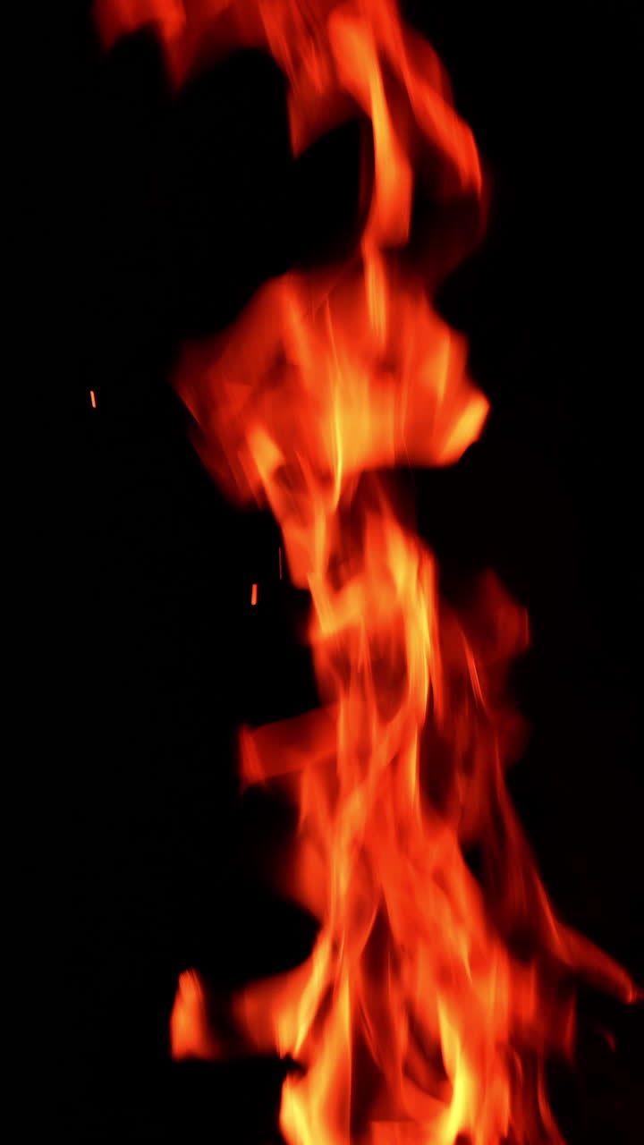 Long and thin flame of the fire burning in the darkness isolated. Tiny sparkles rise up in the air. Vertical video