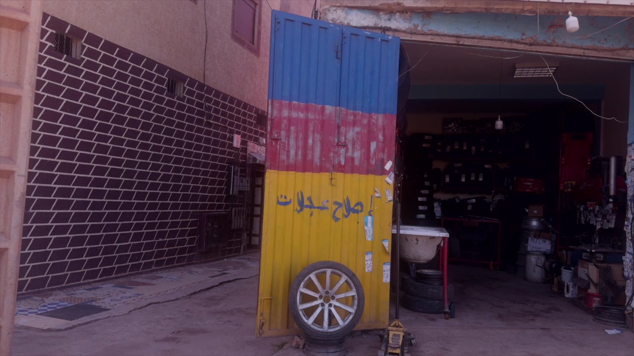 Gommista con insegna blu, rossa e gialla e pneumatico parcheggiato su una strada polverosa marocchina