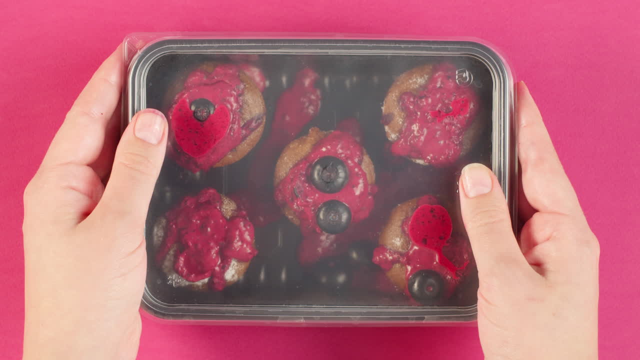 Hands Decorating and Packaging Blueberry Muffins with Pink Frosting