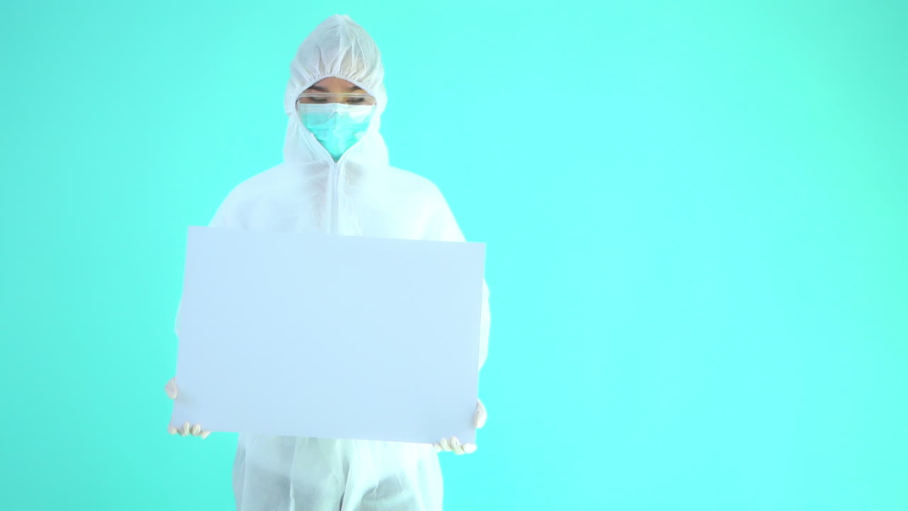 Doctor wearing coverall suit and mask holds white board, chroma key
